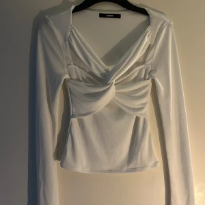 Vit långärmad topp med twist framtill från BikBok - Säljer en vit långärmad topp från BikBok med snygg twistad detalj framtill och v-ringning. Toppen har en figurnära passform och är endast använd två gånger🤍