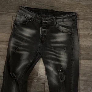 Svarta jeansbyxor från Dsquared2 White Bull - Säljer ett par svarta Dsquared2 White Bull jeans med slitningar och distressed detaljer. Byxorna har fem fickor, dragkedjegylf och en snygg tvättad look. Märkespatch bak på linningen. Perfekta för dig som gillar streetstyle.