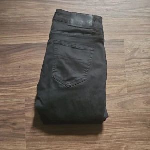 Svarta jeansbyxor från Tiger of sweden  - Säljer ett par svarta jeansbyxor från Tiger of sweden med klassisk femficksdesign och knappgylf. Byxorna har raka ben för en avslappnad passform. Perfekta för dig som gillar en stilren look.