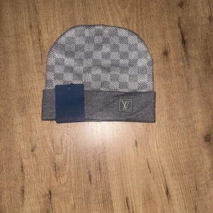 Grå rutig mössa - Snygg grå mössa från med klassiskt rutigt mönster och vikt kant. -logga framtill. Perfekt accessoar för kyliga dagar.