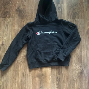 Svart hoodie från Champion - Svart hoodie från Champion med broderad logga på bröstet. Ficka framtill och ribbade muddar vid ärmslut och nederkant. Perfekt för en skön och avslappnad outfit! 💓