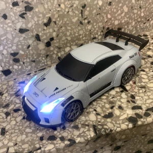 Radiostyrd bil Nissan GT-R med tillbehör - Säljer en radiostyrd bil som liknar en Nissan GT-R i vit färg med svarta detaljer och LED-ljus fram och bak. Medföljer fjärrkontroll, laddkabel, extra koner och tillbehör. Perfekt för racing på hemmabanan! OBS Priset ink frakt