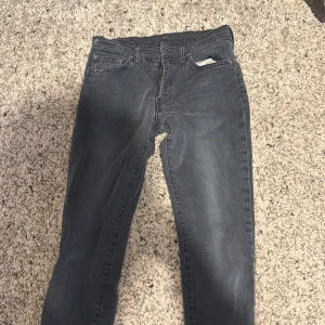 Levis 501 blå jeansbyxor - Klassiska blå/grå Levis  jeans med raka ben och normal passform. Byxorna har fem fickor, knappgylf och tydliga Levis-detaljer som röd etikett och svart läderpatch bak.  Finns en mindre defekt på byxorna i form av färg fäläck (se bild) PRIS KAN DISKUTERAS VID SNABBT KÖP 
