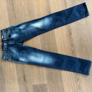 Replay Anbass jeans i blå denim - Säljer ett par Replay Anbass jeans i blå tvättad denim med snygga slitningar. Klassisk femficksmodell med raka ben och normal passform. Jeansen har dragkedjegylf och tydliga Replay-detaljer på bakfickorna. Priset är inte hugget i sten. Hör av er för frågor och prisförslag.