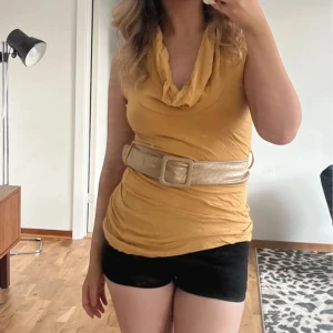 Gul topp med stor krage och bredt bälte - Toppen är ärmlös och har en figurnära passform. Perfekt för dig som vill sticka ut med en färgglad och unik look. Toppen passar jättebra till utlandsvistelsen 🐆