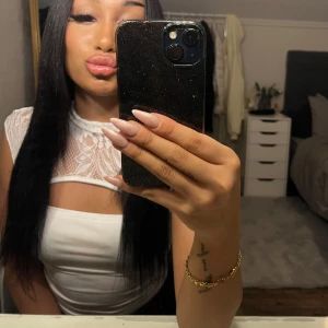 Vit topp med spetsdetaljer - Säljer en vit topp med genomskinliga spetsdetaljer upptill och hög hals. Toppen är ärmlös och har en tight passform som framhäver figuren. Ryggen är spets och ogenomskinlig Perfekt för att lyfta en outfit med en elegant touch.