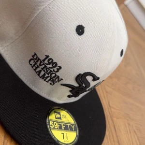 Vit och svart keps från New Era 59FIFTY - Säljer en vit och svart 59FIFTY keps från New Era med broderad text '1993 Division Champs' och White Sox-logga framtill. MLB-logga baktill. Klassisk flat peak och broderade ventilationshål.