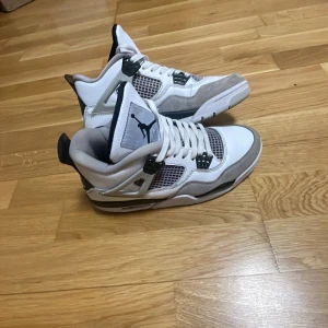 Nike Air Jordans vita och grå sneakers - Säljer ett par Nike Air Jordans i vitt och grått med svarta detaljer. Skorna har klassisk mesh på sidorna, snörning och rund tå. Perfekta för dig som gillar streetwear och vill ha en ikonisk sneaker i garderoben.