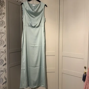 Ljusblå långklänning från vila  - Säljer en elegant ljusblå långklänning från vila i satinliknande material. Klänningen är ärmlös med v-ringad draperad front och har en stilren, slät baksida. Perfekt för speciella tillfällen. Aldrig använt pris lapp finns original priset ligger på 500kr