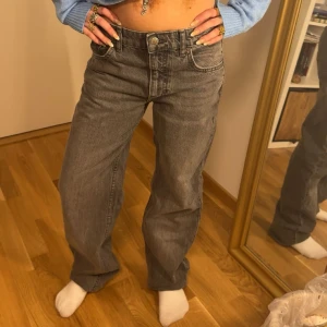 Grå jeansbyxor med rak passform - Säljer ett par grå jeansbyxor med normal passform och raka ben. Klassisk femficksmodell med knapp och dragkedja framtill. Perfekta för en avslappnad och stilren look. Lågmidjade och toppen kommer med