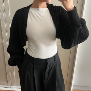 Svart ribbad bolerotopp - Säljer denna svarta, ribbstickade bolerotopp från Stockh LM. Den är supermjuk och har ett stretchigt material, perfekt att slänga över något kortärmat. I väldigt fint skick.  Material: 50 % bomull, 50 % akryl.