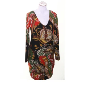 Färgstark retroklänning med djup ringning & mönster i svart, rött & grönt, Stl Small/36 Vintage  - Märkt XL men sitter som en liten S. Stretchig 2000-talsklänning med färgstarkt retromönster i svart, rött och grönt. Djup ringning och lång ärm, passar perfekt både till vardags och fest. Mycket fint skick – inga synliga defekter. Ingen prutning, men bundlerabatt erbjuds!  