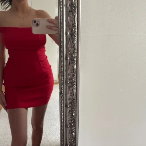 Röd axelbandslös klänning från ASOS DESIGN - Säljer en röd axelbandslös klänning från ASOS DESIGN. Klänningen är tight och kort, med en stilren och enkel design. Perfekt för dig som vill sticka ut med en färgstark look. Dragkedja i baksidan för enkel påklädning.