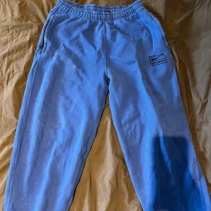 Blå mjukisbyxor från Nike - Säljer ett par blå mjukisbyxor från Nike med resår i midjan och fickor på sidorna. Byxorna har en enkel design med Nike-logga på vänster ben och är perfekta för en avslappnad stil. Finns några små fläckar på den som säkert går bort k tvätten. Pris nu 2000kr.