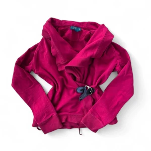 Omlottkofta - Säljer en snygg röd omlottkofta från Ralph lauren med bälte i midjan. Koftan har långa ärmar och är perfekt för lager-på-lager-stil. Passar både till jeans och kjol.