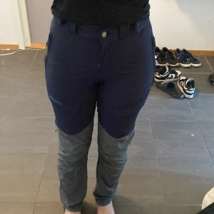 Mörkblå och grå friluftsbyxor med dragkedjor - Säljer ett par  friluftsbyxor med praktiska dragkedjor på sidorna och förstärkta partier på knän och bak. Och flera fickor för förvaring.Helt nya 