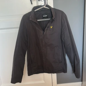 Mörkbrun jacka från Lyle & Scott - Säljer en stilren mörkbrun jacka från Lyle & Scott med dragkedja och klassisk krage. Jackan har lång ärm, två sidofickor. Priset kan diskuteras! 