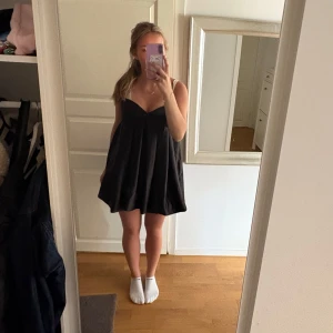 Svart kortklänning med smala axelband - Säljer en svart kortklänning med smala axelband och v-ringning. Klänningen har en lös passform och är perfekt för varma dagar. Enkel och stilren design som passar till många tillfällen.