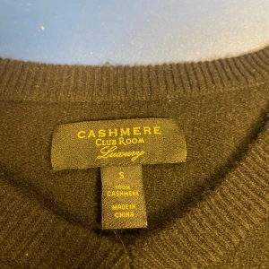 Svart kashmirtröja från Club Room - Mjuk och lyxig svart tröja i 100% kashmir från Club Room. Klassisk V hals och långa ärmar. Perfekt för dig som vill ha en stilren och bekväm tröja i garderoben.