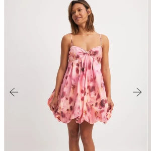 NA-KD rosa klänning - Superfin kortklänning i rosa nyanser med blommigt mönster och ballongliknande kjol. Klänningen har tunna axelband och en twistad detalj vid bysten som ger en söt touch. Perfekt för sommarens alla tillfällen!