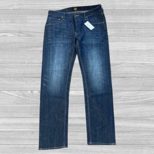 Lee jeans - Säljer ett par klassiska mörkblå jeans från Lee med raka ben och femficksdesign. Byxorna har orangea sömmar och en läderpatch bak i midjan. Perfekta för dig som gillar en tidlös och enkel stil.