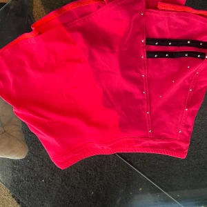 Rosa kjol från Passionice - Säljer en knallrosa kjol från Passionice med svarta dekorband och små silvriga nitar som detalj. Kjolen är i stretchigt material och är perfekt för dig som gillar färg och att sticka ut. Den ser också jättefin ut när du hoppar på isen. Kjolen är ungefär 150-160 i strl. Skriv till mig för fler frågor😊🫶🩷