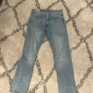 Levis 501 ljusblå jeans - Klassiska Levis 501 jeans i ljusblå denim med raka ben och femficksmodell. Byxorna har knappgylf och den ikoniska Levis-lappen bak i midjan. Perfekta för en avslappnad stil.