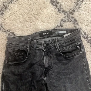 Replay Anbass svarta jeans - Säljer ett par Replay Anbass jeans i svart tvätt med klassisk femficksdesign och raka ben. Jeansen har snygga detaljer vid fickorna och en diskret Replay-logga. Perfekta för dig som gillar en stilren look. Helt nya