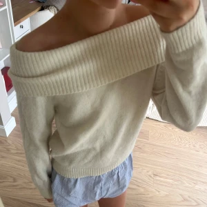 Offshoulder vit stickad tröja - Säljer en superfin offshoulder vit stickad tröja med bred ribbad kant upptill. Perfekt för dig som vill ha en stilren och trendig look. Tröjan är mjuk och skön, passar till många olika outfits.