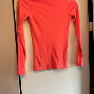 Korallrosa långärmad topp från Gina Tricot - Säljer en enkel och snygg korallrosa långärmad topp från Gina Tricot. Modellen är figurnära med rund halsringning och tillverkad i mjuk bomull. Perfekt att styla med jeans eller kjol. Lite nopprig (se bild 3) 