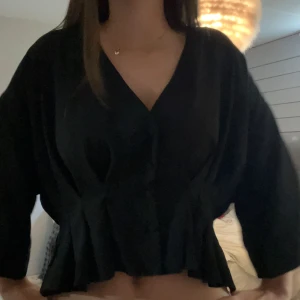 Söt Svart blus med knappar och v-ringning💕 - Säljer en svart blus med v-ringning och knappar framtill. Blusen har lös passform, trekvartsärmar och en lätt volang nertill. 