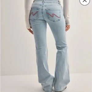 Populära slutsålda Nelly Ljusblå bootcut jeans med slitningar - Säljer ett par ljusblå bootcut jeans med slitna detaljer vid knäna och broderade bakfickor. Jeansen har hög midja och klassisk femficksdesign. Perfekta för dig som gillar en avslappnad men trendig look. Storlek 32 och passar om du är ca 158-168 cm.