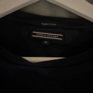 Mörkblå långärmad tröja från Tommy Hilfiger - Säljer en stilren mörkblå långärmad tröja från Tommy Hilfiger i ekologisk bomull. Tröjan har en klassisk passform och en liten broderad logga på bröstet. Perfekt basplagg för garderoben.