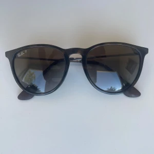 RayBand solglasögon - Klassiska svarta solglasögon från Ray-Ban med rundade bågar och tunna metallskalmar. Snygg och tidlös design med mörka glas. Perfekta för soliga dagar och passar till de flesta stilar. Det är bara att fråga om du undrar något!