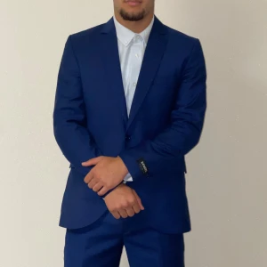 Blå kostym från Kenzel For Men - Säljer en stilren blå kostym från Kenzel For Men. Kostymen har en klassisk kavaj med knappar och matchande byxor. Materialet är en blandning av ull och viskos, vilket ger en snygg och bekväm känsla. Perfekt för bal eller student. Den säljs även komplett för ett rimligt pris//frågor eller intresserad->dm