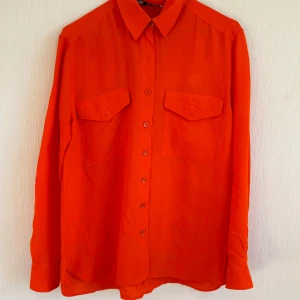 Orangeröd skjorta från Zara - Säljer en snygg orangeröd skjorta från Zara i storlek S. Skjortan har klassisk krage, två bröstfickor med lock och knäppning framtill. Perfekt för dig som vill sticka ut med färg! 💥