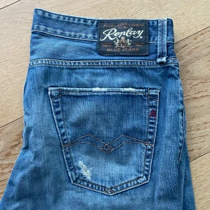 Blå Replay jeans med raka ben - Säljer ett par klassiska blå jeans från Replay med raka ben och snygga slitningar. Jeansen har fem fickor, tydlig Replay-logga på bakfickan och läderpatch bak i midjan. Perfekta för dig som gillar en tidlös jeanslook. Pris kan diskuteras!