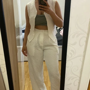Vit quiltad väst - Säljer en vit quiltad väst med struktur och utan ärmar. Västen har en klassisk passform och är perfekt för att ge din outfit en trendig touch. Passar snyggt över en topp eller skjorta.