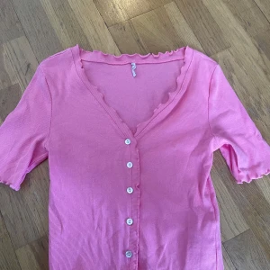Rosa ribbad topp från ONLY - Säljer en söt rosa ribbad topp från ONLY med v-ringning och vita knappar framtill. Toppen har korta ärmar och volangkant vid halsringningen för en extra detalj. Använd två gånger och är i väldigt bra skick, även perfekt till sommaren!💗🌸