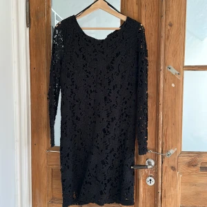 Svart spetsklänning från Wera - Säljer en svart klänning från Wera med vackert blommigt spetsmönster. Klänningen har lång ärm och rak passform, perfekt för dig som gillar stilrena detaljer och elegant look. Fodrad inuti för extra komfort.