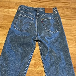 Levi's Ribcage Straight Ankle jeans - Säljer ett par klassiska blå Levi's Ribcage Straight Ankle jeans med raka ben. Jeansen har fem fickor, knappgylf och den ikoniska Levi's-detaljen bak. Perfekta för en avslappnad och stilren look. Storlek W26!