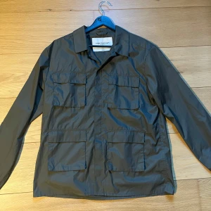 Grön vindjacka/overshirt från These Glory Days - Säljer en stilren grön vindjacka/overshirt från These Glory Days. Jackan har fyra stora fickor framtill, klassisk krage och stängs med knappar. Perfekt för dig som gillar enkel och funktionell design.