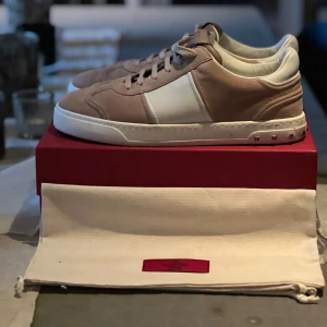 Valentino flycrews i Beige och vita sneakers från Valentino - Säljer ett par snygga sneakers från Valentino i beige mocka med vita detaljer och vit sula. Skorna har snörning och en klassisk rund tå. Perfekta för dig som vill ha en stilren och exklusiv look. Pris kan diskuteras. Och har allt som kan komma med.