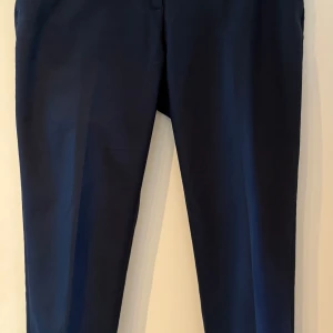 Mörkblå kostymbyxor från H&M - Snygga mörkblå ankelkorta kostymbyxor från H&M med klassisk rak passform. Perfekta till en stilren look och enkla att matcha med olika toppar. Slits längs ner i benen. Sömmen längs ner i ena benöppningen har gått upp lite. Jag är inte bra på att sy så överlämnar det till köparen att ta sig an 😊🌸