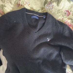 Svart v-ringad tröja från GANT - Klassisk svart v-ringad tröja från GANT med diskret broderad logga på bröstet. Tröjan har långa ärmar och är tillverkad i mjuk ullblandning. Perfekt för en stilren och enkel look. Den är S men tvättad så mer XXS- Xs