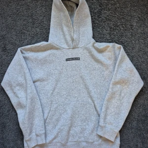 Grå hoodie från Calvin Klein Jeans - Snygg ljusgrå hoodie från Calvin Klein Jeans med svartvit logga på bröstet och liten 'ck'-brodyr på ärmen. Klassisk känguruficka och hyva. Perfekt för en avslappnad stil. Priset kan alltid diskuteras😁