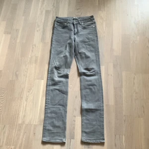 Grå jeansbyxor från Acne Jeans storlek 26 32 - Säljer ett par grå jeansbyxor från Acne Jeans med klassisk femficksdesign och raka ben. Byxorna har normal passform och är tillverkade i ett mjukt jeanstyg. Perfekta för dig som gillar stilrena och enkla jeans.