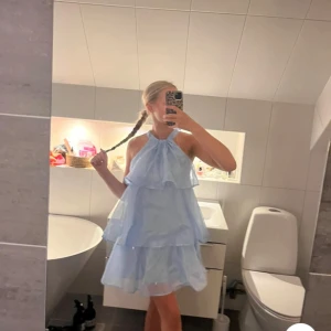 Ljusblå volangklänning med halterneck - Säljer en söt ljusblå klänning med volanger och halterneck. Klänningen har flera lager och en luftig passform, perfekt för varma dagar. Den är ärmlös och har en kort längd som ger en fräsch och somrig look.