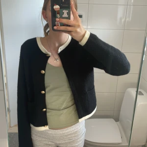 Svart cardigan jacka med vita detaljer från Zara - Säljer en svart cardigan jacka från Zara med vita kanter och guldiga knappar framtill. Bra skixk då jag ej använt den så många gånger 