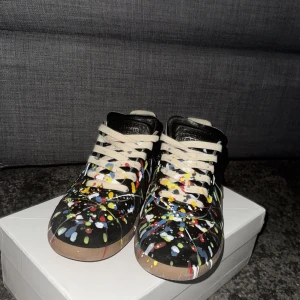 Maison Margiela sneakers med färgstänk - Unika svarta sneakers från mason margiela med färg stänkt på. Skorna e använd nån enstaka gång så där! Skorna e ftf toppskick ser knappt att de har används!!!😎 Box och tillbehör ingår🍾🙌🏼🙌🏼🍾 perfekt nu till sommaren